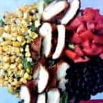 corn, black beans, salad, tomato, and chicken breast in a clear glass bowl