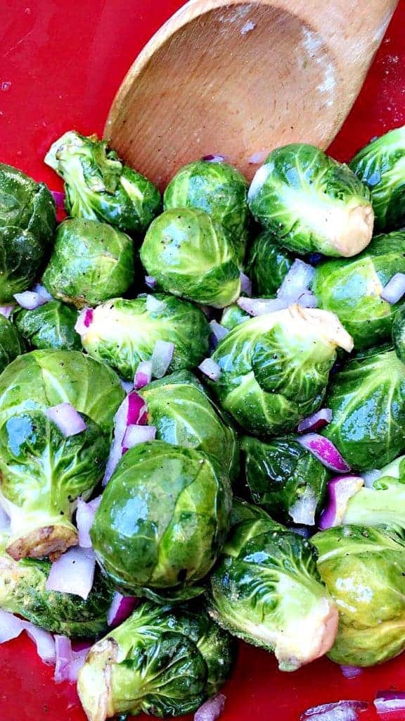 close up of red bowl with brussels sprouts and onions and a wooden spoon