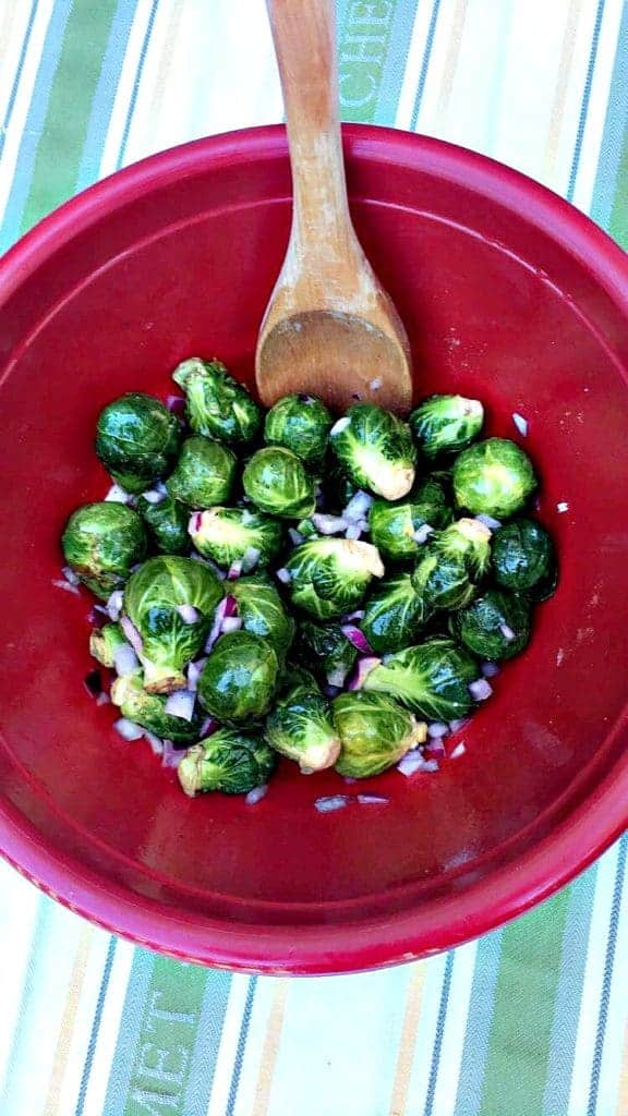red bowl with brussels sprouts and onions and a wooden spoon