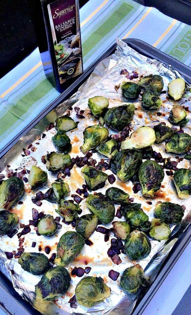 roasted brussels sprouts on a foil lined baking sheet with a bottle of balsamic