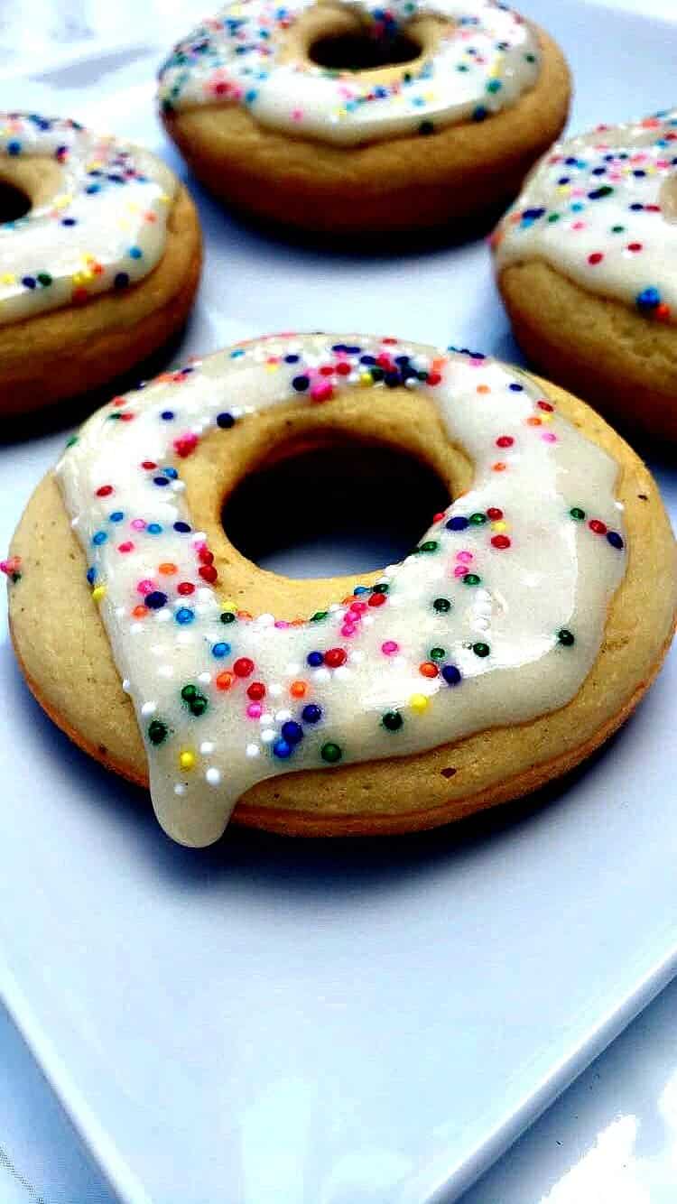 4 vanilla protein donuts on a white plate with sprinkles