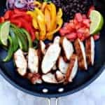 skillet with chicken breasts, veggies, black beans and lime