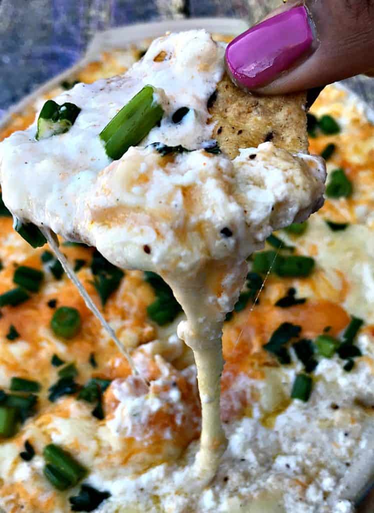 person holding a bite of hot crab dip with a chip