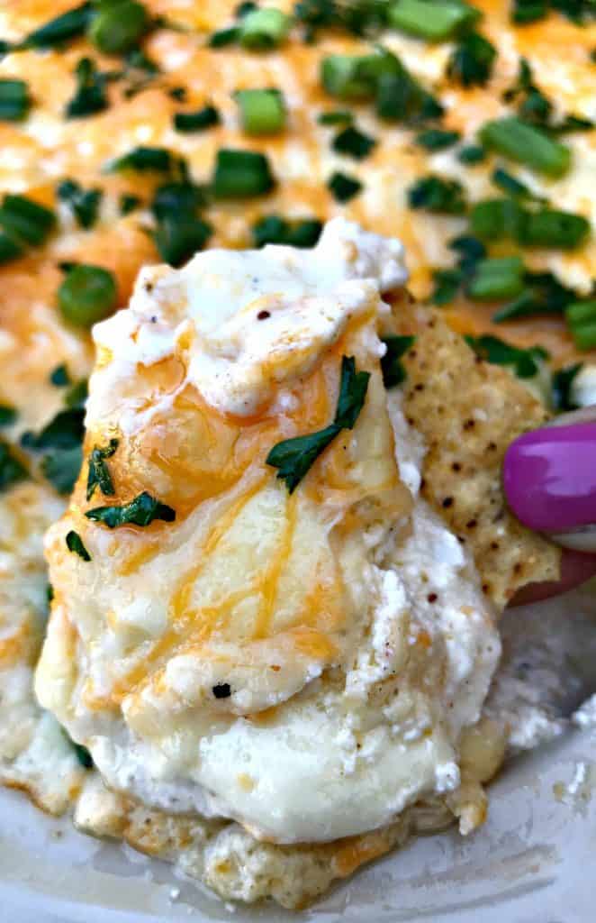 person holding a bite of hot crab dip with a chip