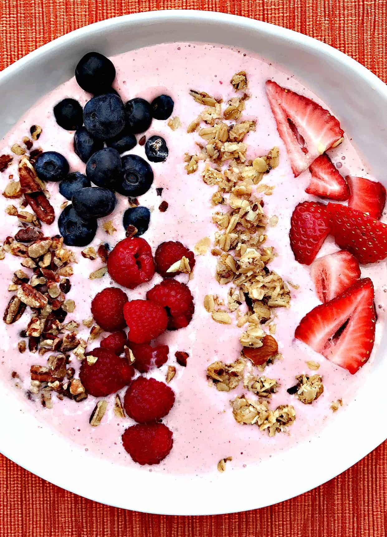 almond butter berry power protein smoothie topped with granola, blueberries, raspberries, and sliced strawberries in a white bowl