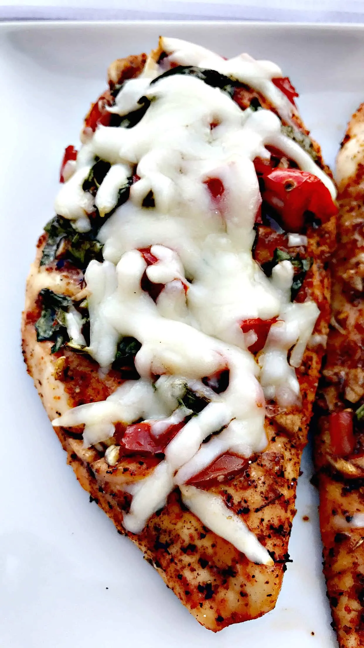 close up of bruschetta stuffed chicken breast on a white plate