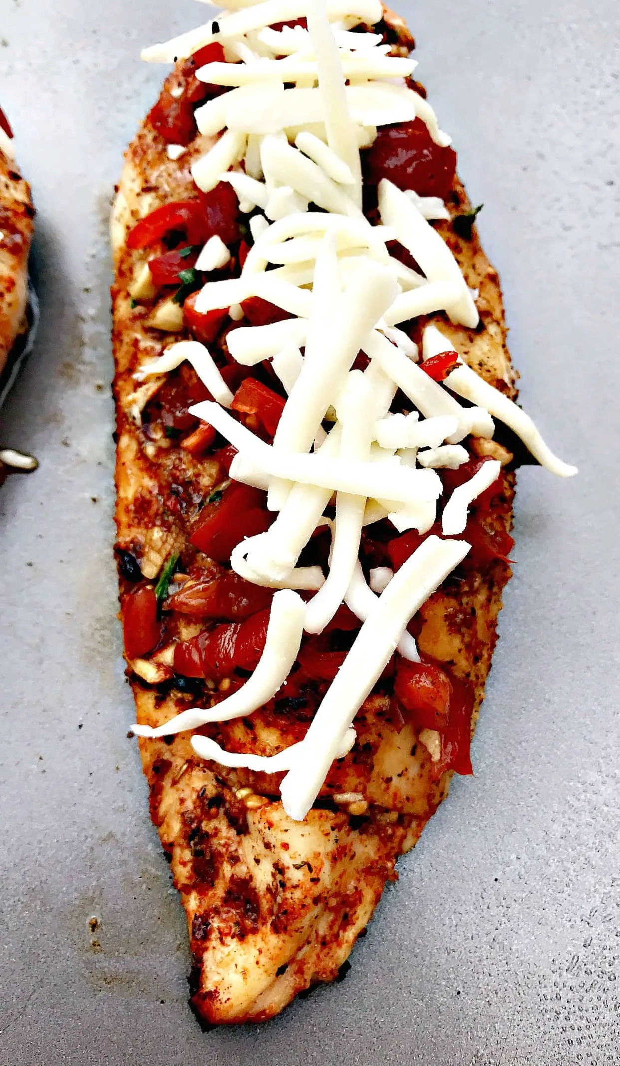 close up of bruschetta stuffed chicken with shredded cheese on a baking sheet