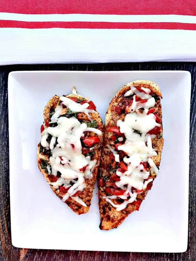 bruschetta stuffed chicken on a white plate with a red and white napkin