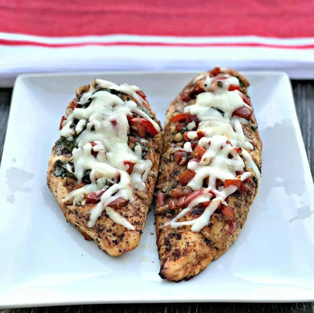 bruschetta stuffed chicken on a white plate with a red and white napkin
