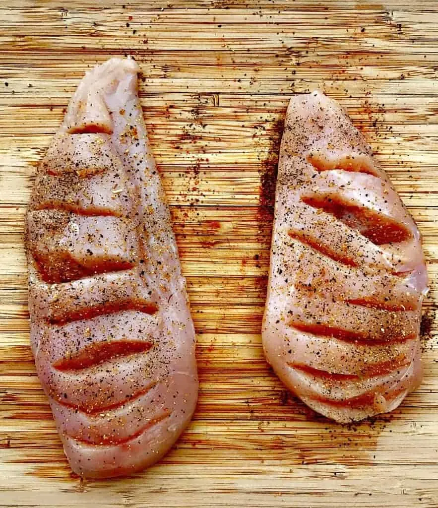 raw chicken breasts on a cutting board sliced for stuffing