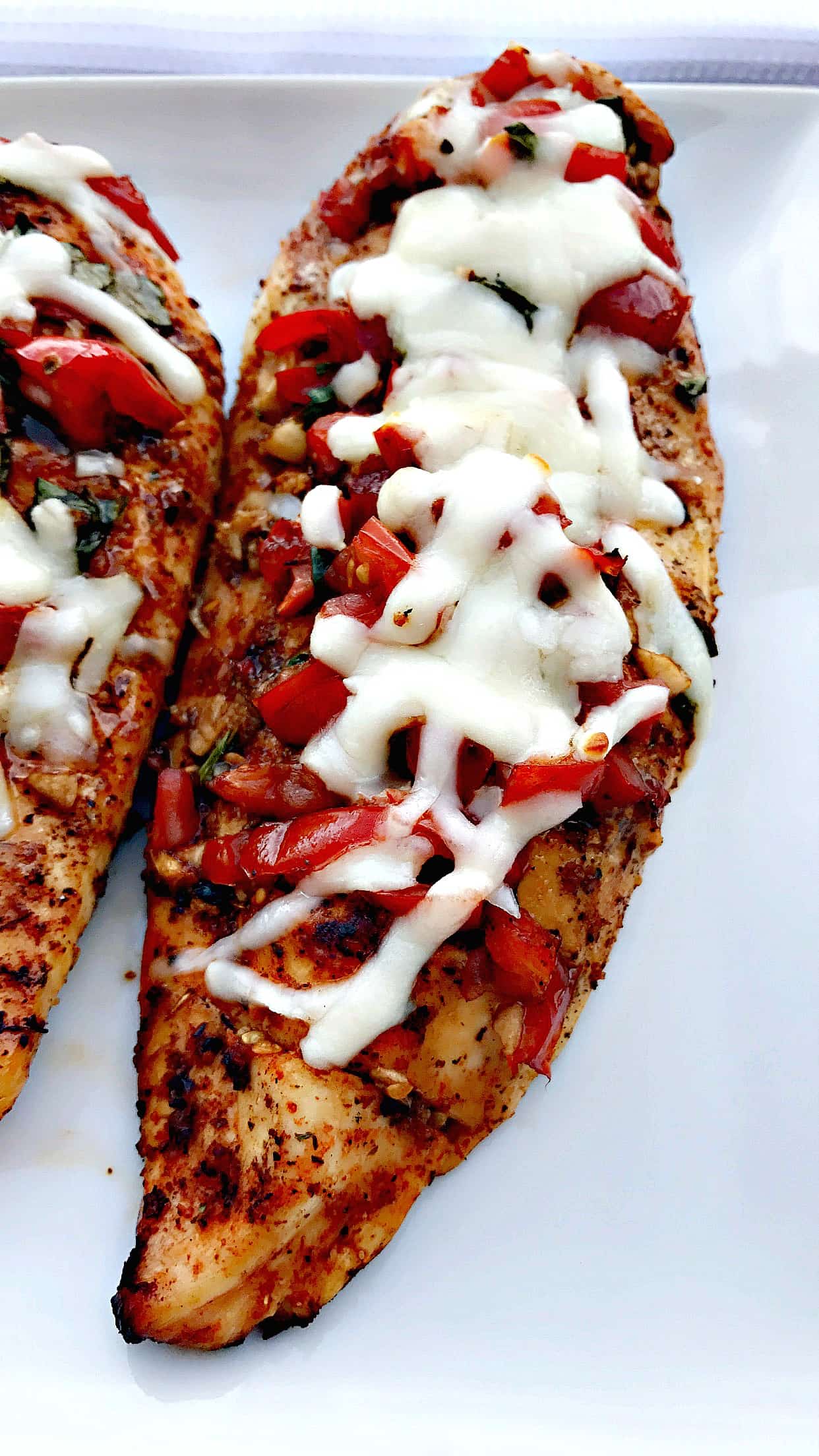 close up of bruschetta stuffed chicken breast on a white plate