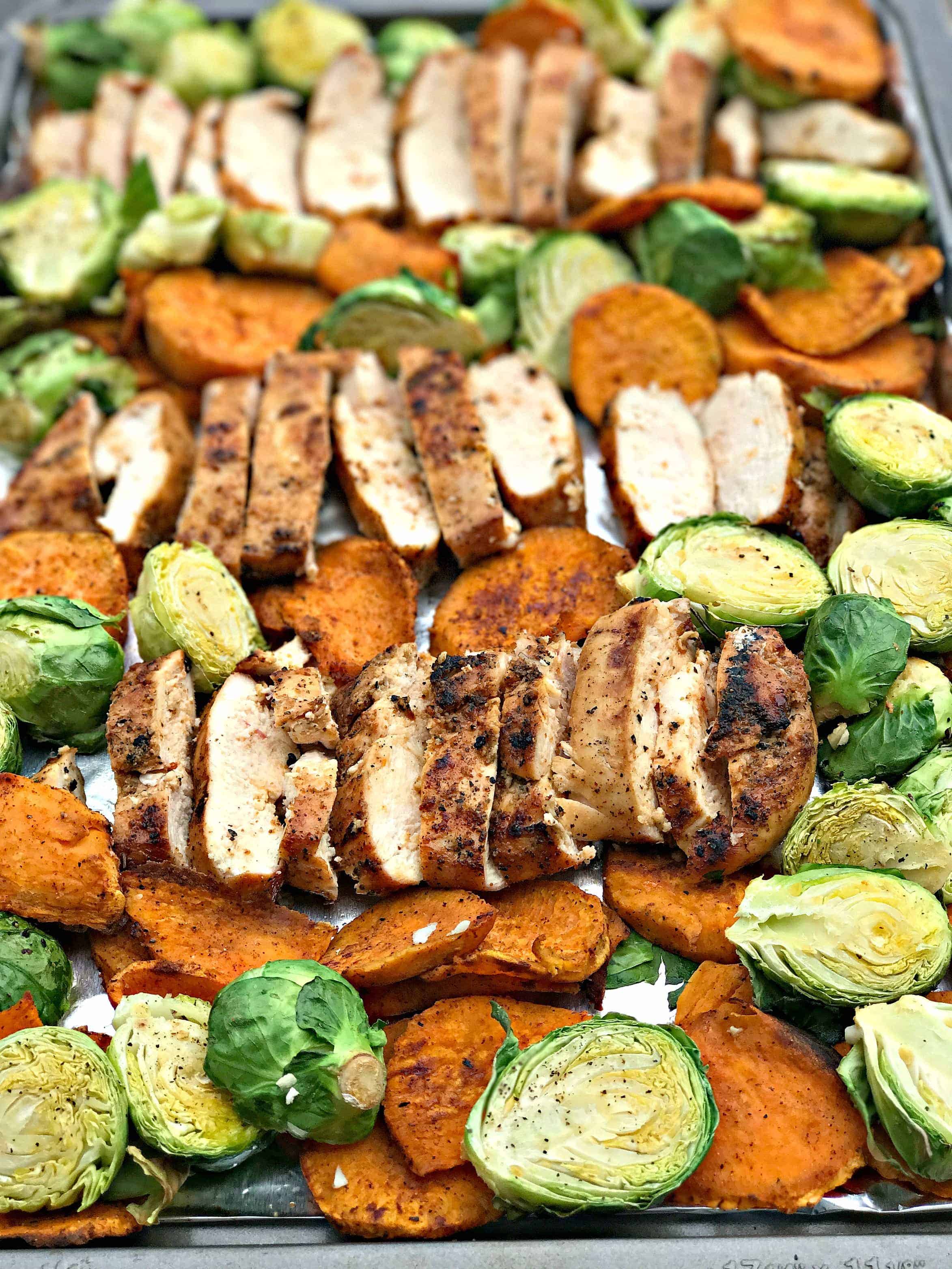 sliced chicken breasts, sweet potatoes, brussels sprouts on a baking sheet