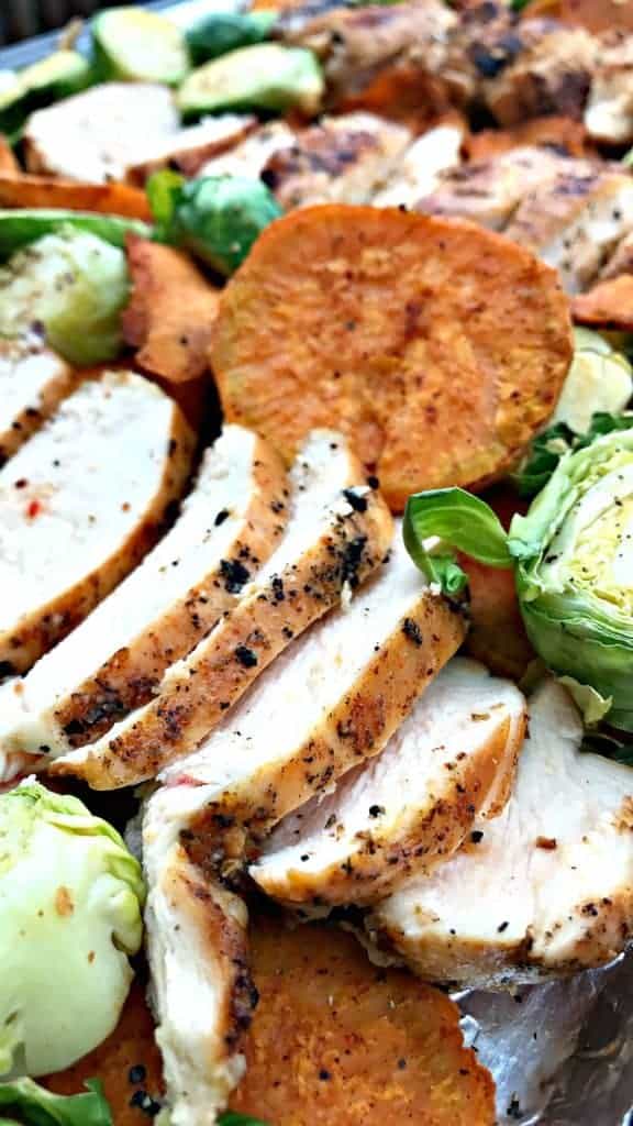 close up of chicken and sweet potatoes and brussels spouts on a baking sheet