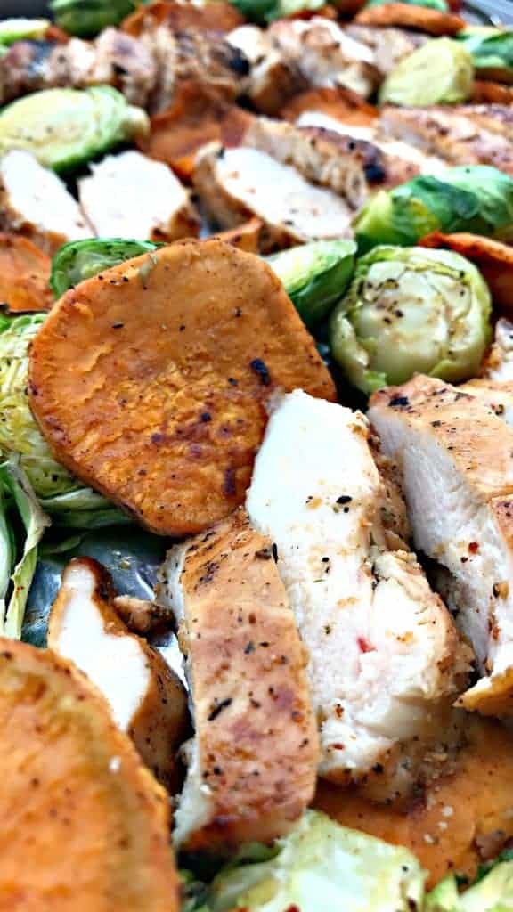 close up of chicken and sweet potatoes and brussels spouts on a baking sheet