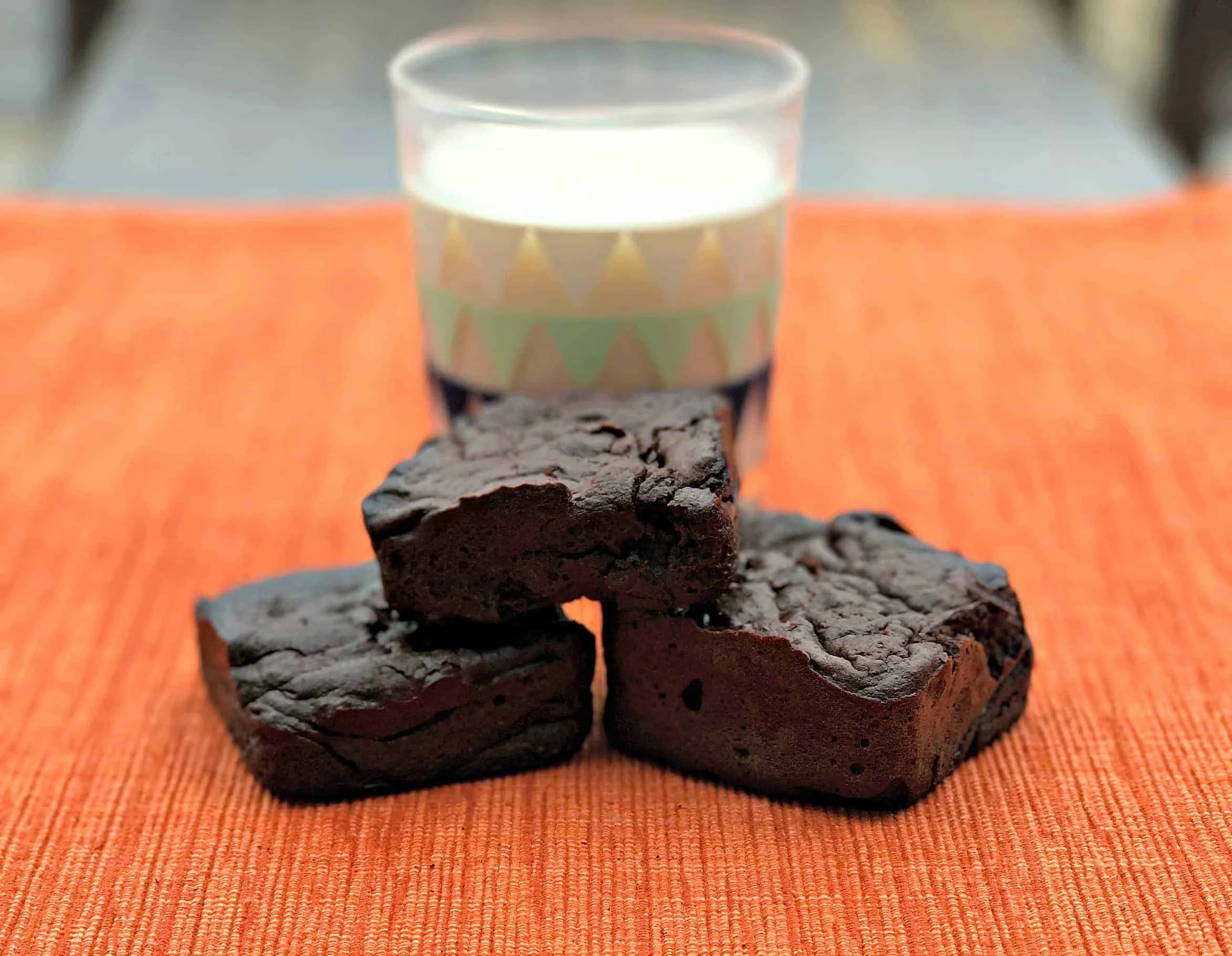 3 brownies stacked in front of a glass of milk