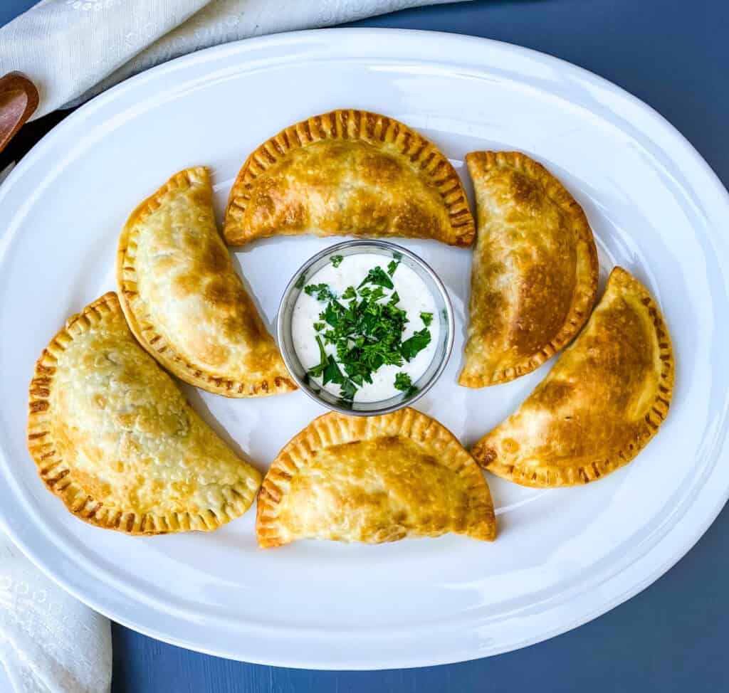 beef empanadas on a white plate with white sauce and cilantro