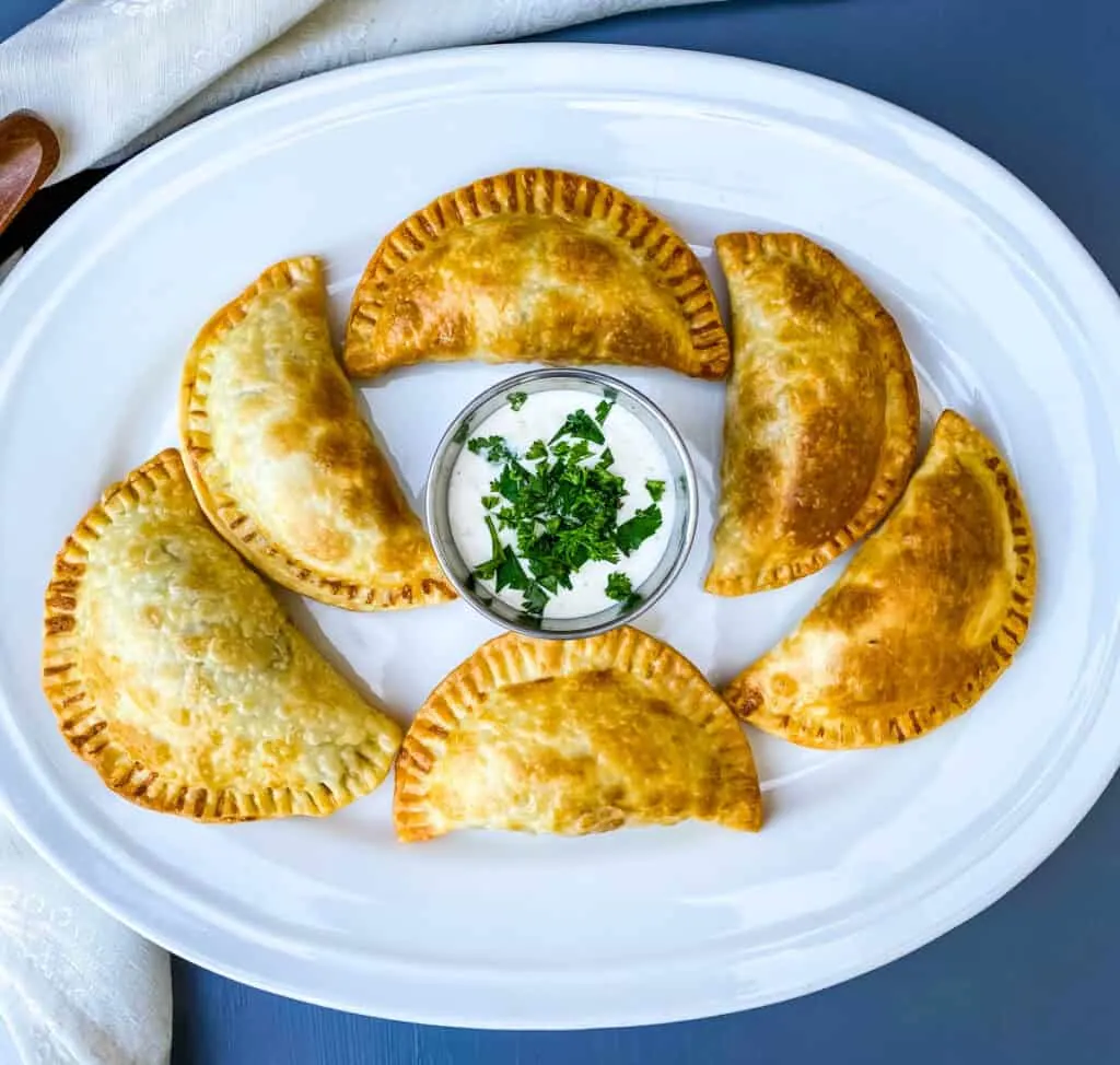 beef empanadas on a white plate with white sauce and cilantro