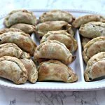 beef empanadas on a white plate with white sauce and cilantro