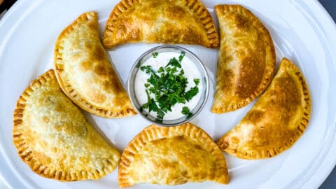 beef empanadas on a white plate with white sauce and cilantro