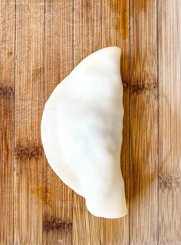 uncooked beef empanada on a bamboo cutting board