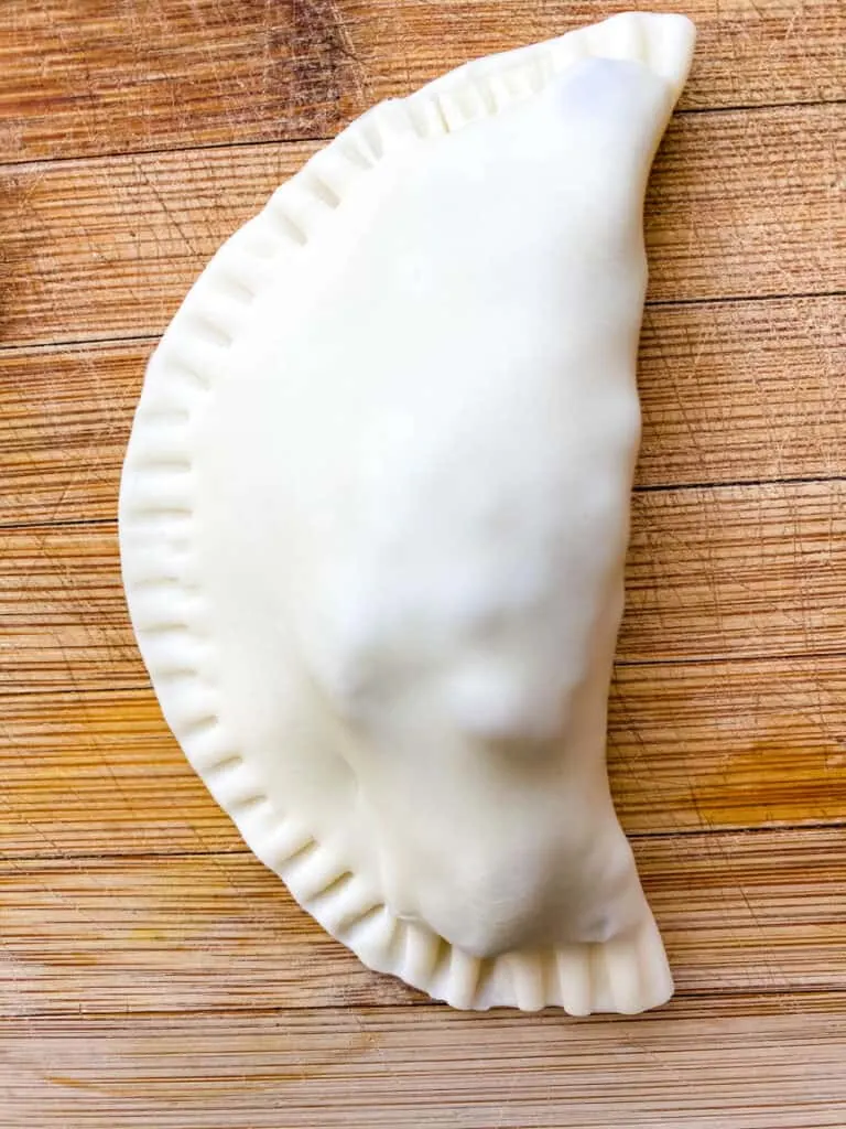 uncooked beef empanada on a bamboo cutting board