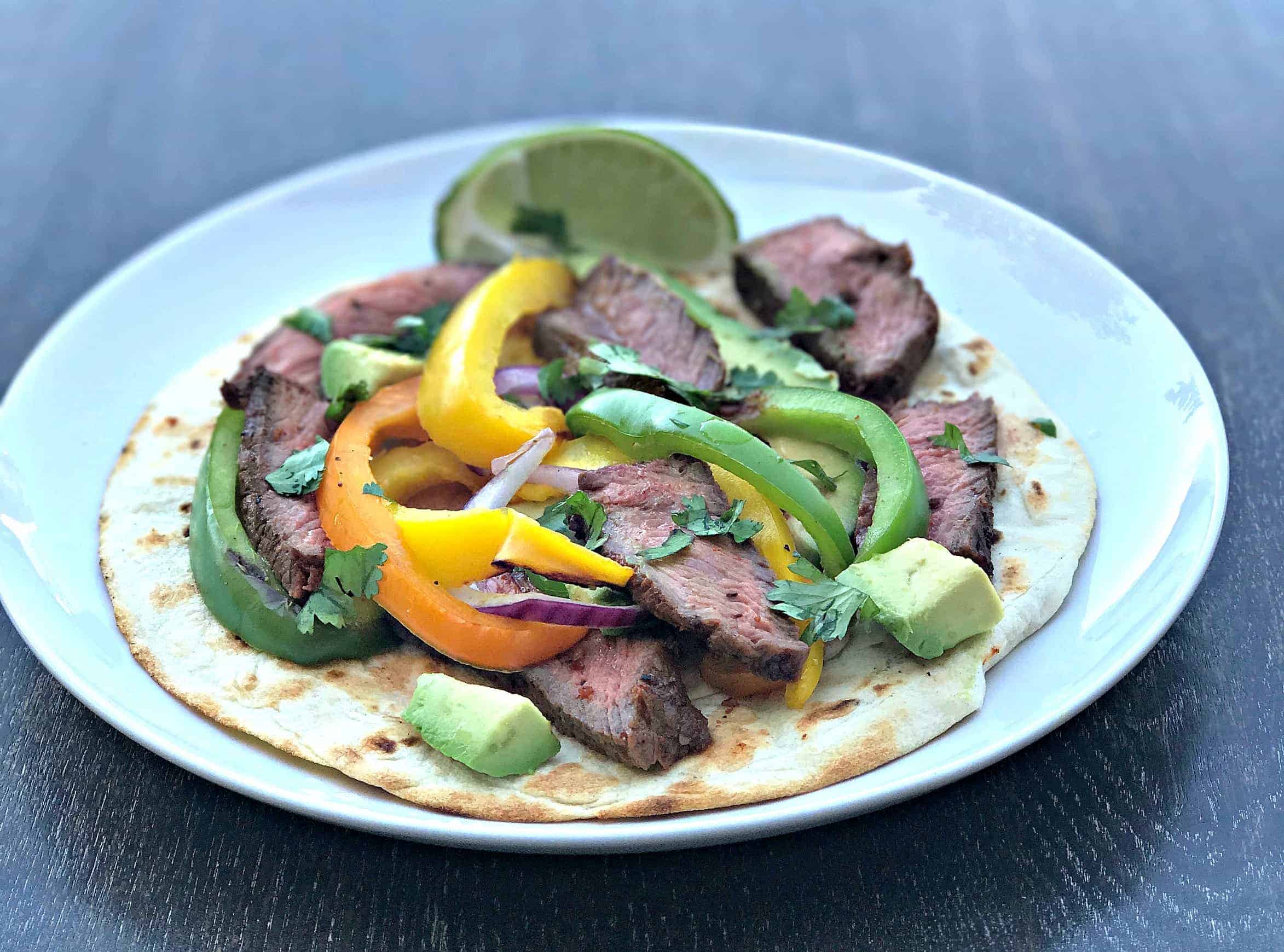 grilled steak fajitas on a tortilla on a white plate