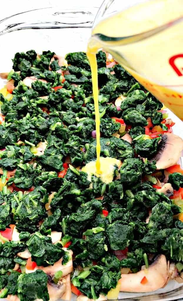 raw egg being poured into a dish with vegetable ingredients for Low-Carb Bacon, Egg, and Spinach Breakfast Casserole in a glass pan