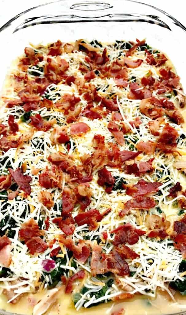 bacon, cheese, and vegetable ingredients for Low-Carb Bacon, Egg, and Spinach Breakfast Casserole in a glass pan