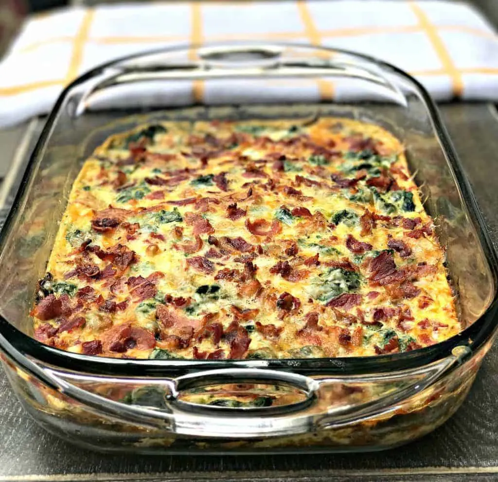 Low-Carb Bacon, Egg, and Spinach Breakfast Casserole in a glass pan with a white and yellow napkin