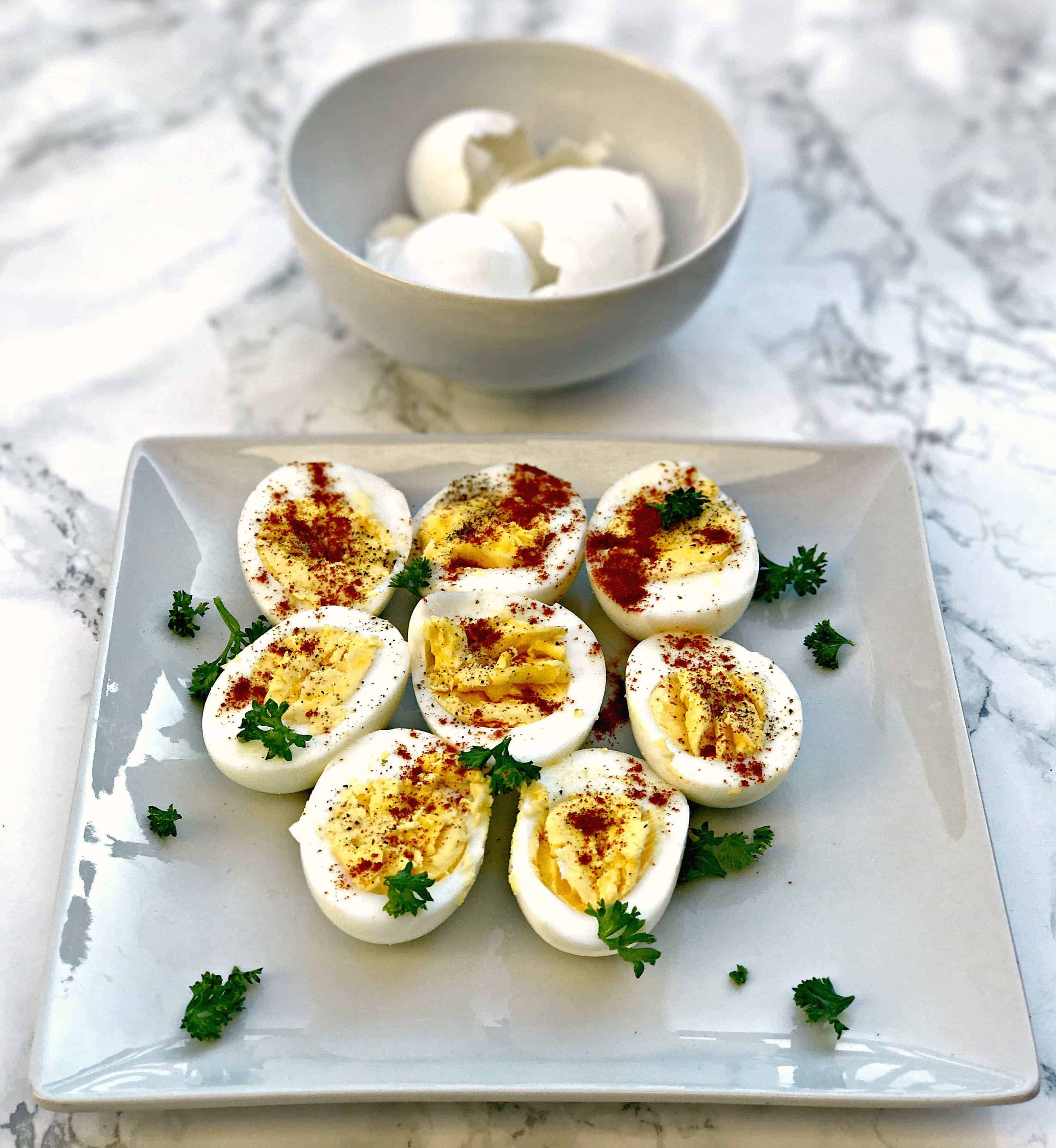 sliced hard boiled eggs on a square plate and a bowl of peeled egg shells