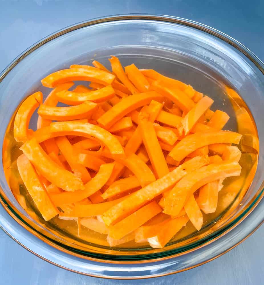 raw sweet potatoes sliced and in a glass bowl filled with water