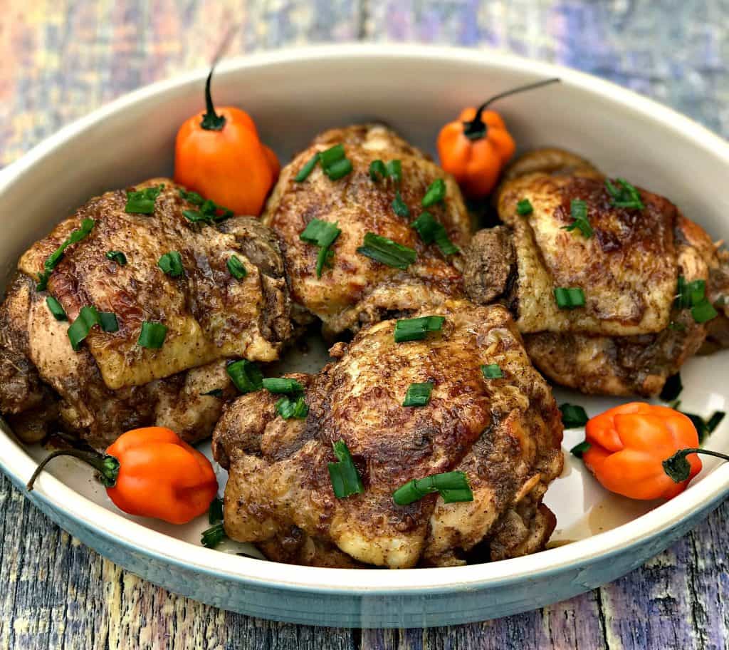 Jamaican jerk chicken thighs on a serving platter garnished with green onions and habanero peppers