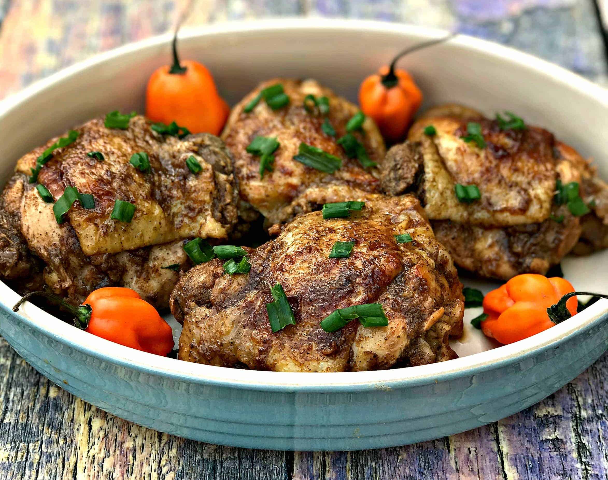 Jamaican jerk chicken thighs on a serving platter garnished with green onions and habanero peppers