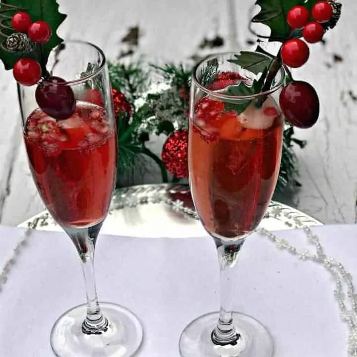 2 champagne flutes containing pomegranate mimosas, pomegranate seeds, and holiday decor
