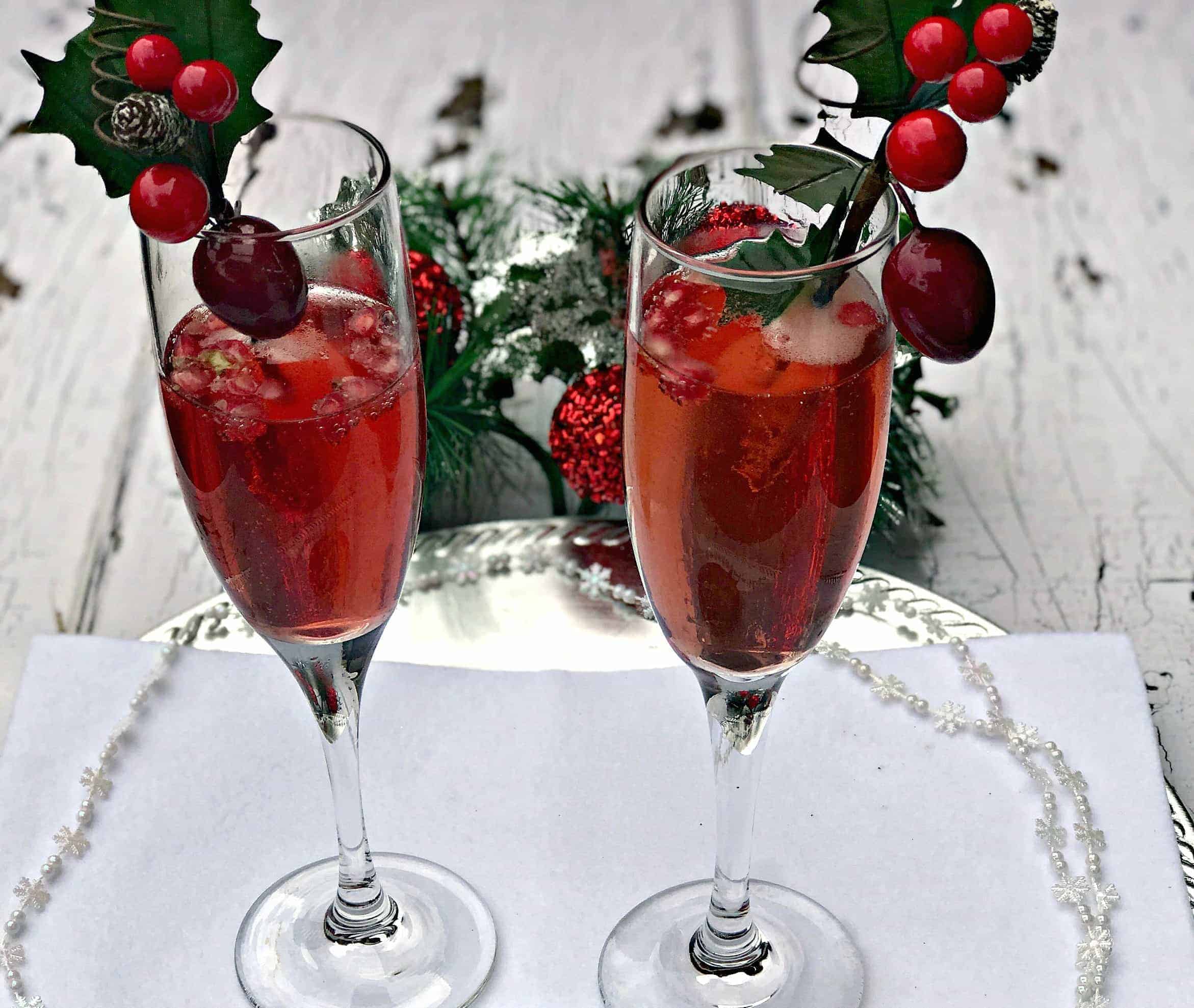 2 champagne flutes containing pomegranate mimosas, pomegranate seeds, and holiday decor