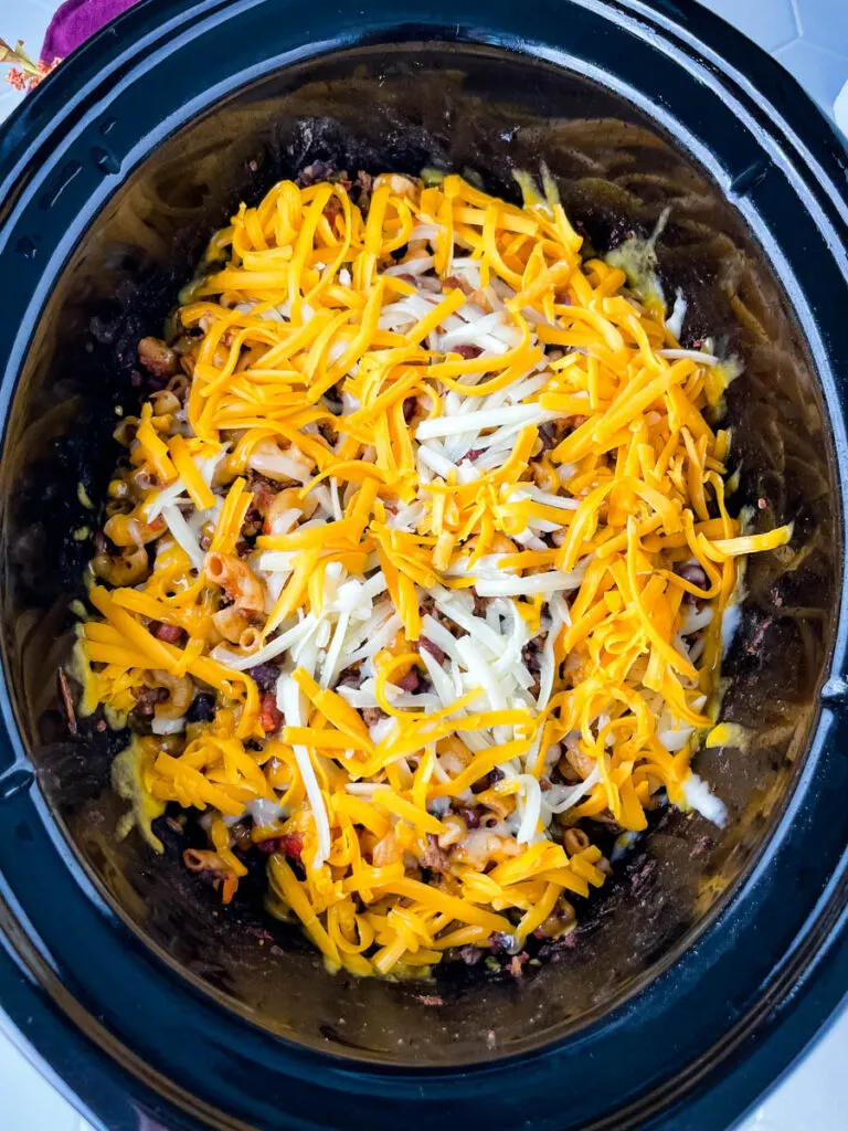 uncooked chili mac and cheese in a slow cooker topped with cheese