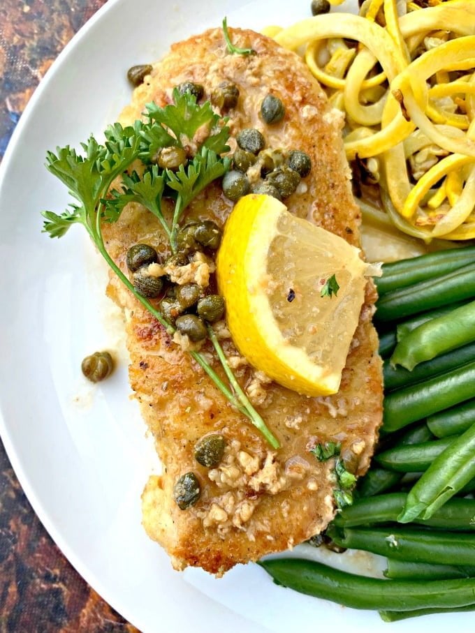 keto lemon chicken piccata on a white plate with green beans and squash