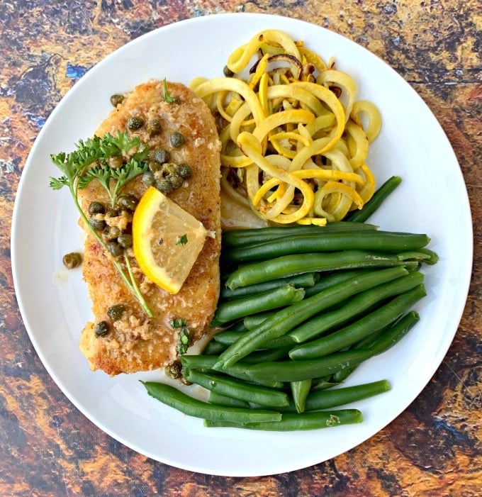 keto lemon chicken piccata on a white plate with green beans and squash