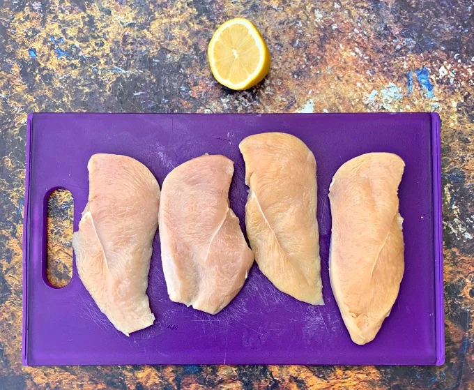 raw chicken breasts on a purple cutting board with a lemon
