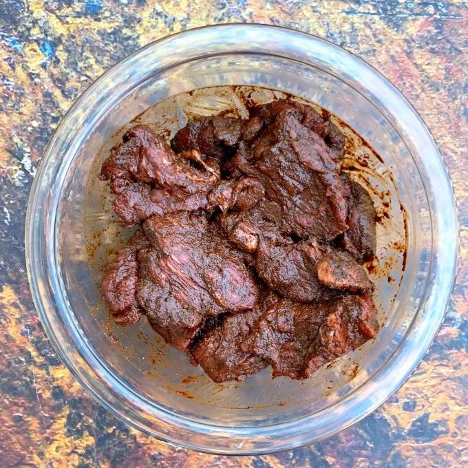raw steak in a bowl with homemade fajita seasoning and marinade