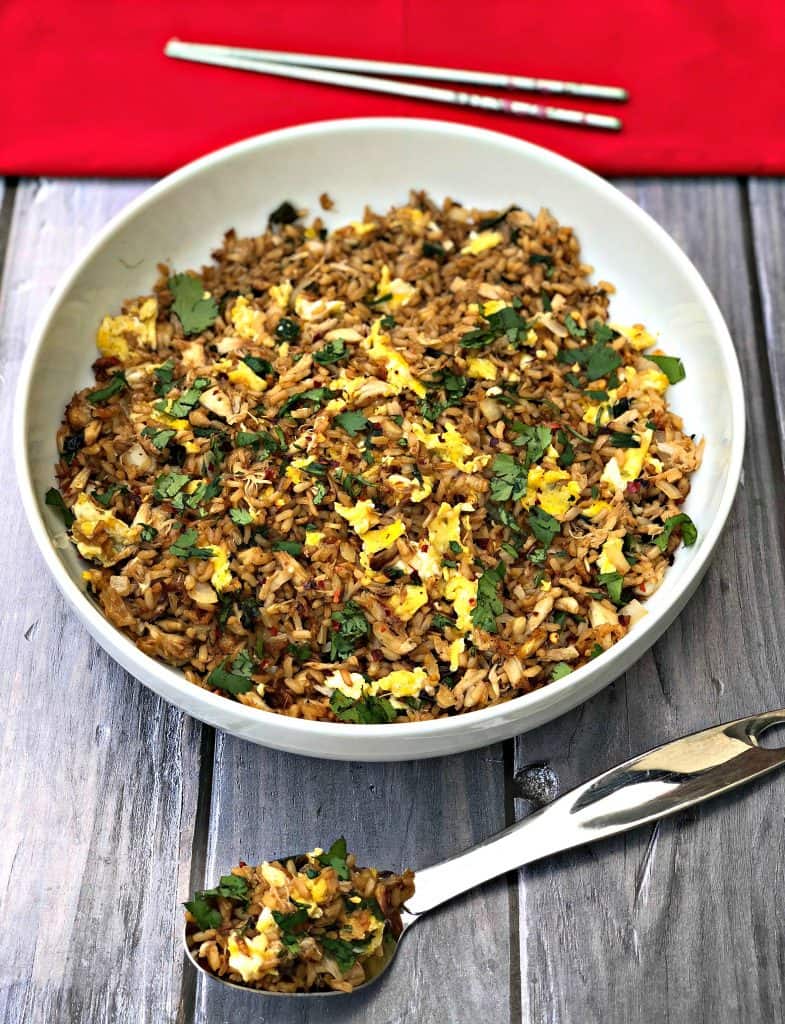 Air Fryer Crab Fried Rice in a white bowl with a large spoon of rice on a dark surface with a red napkin and chopsticks