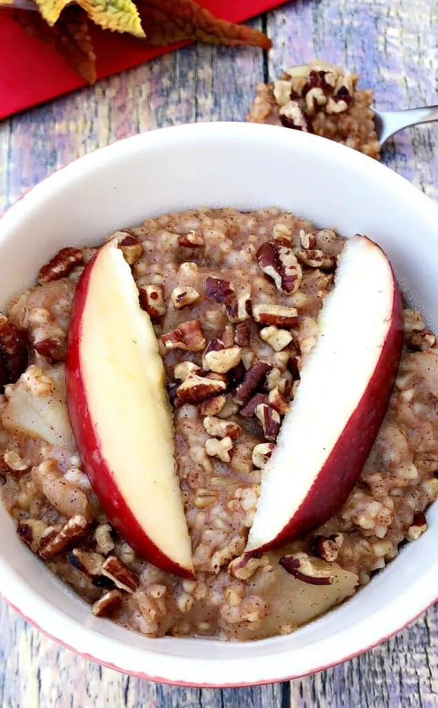 Instant Pot Apple Pie Steel Cut Oats in a red bowl with a fresh apple and red napkin