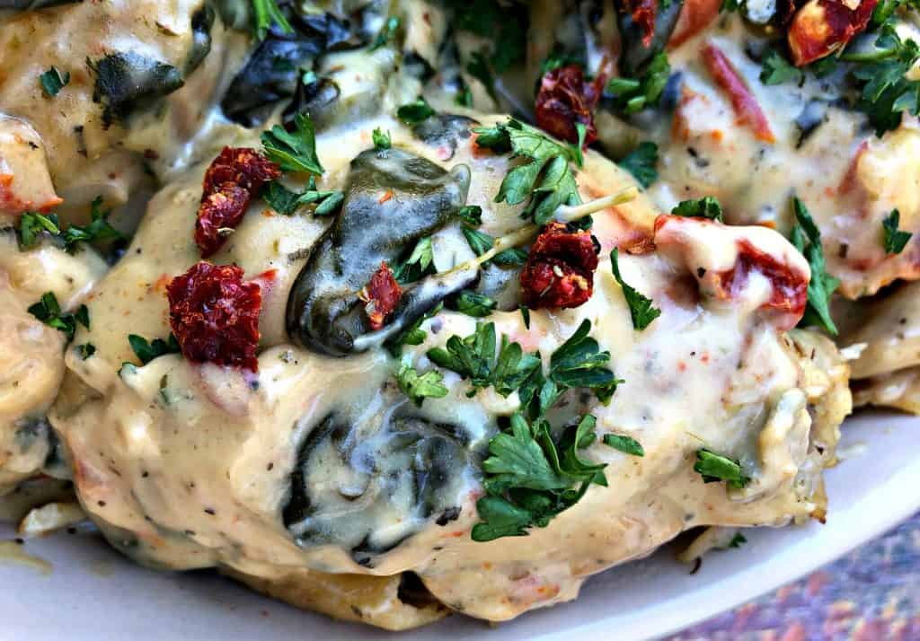 close up photo of Instant Pot Low-Carb Creamy Garlic Tuscan Chicken Thighs in creamy sauce with parsley in a bowl