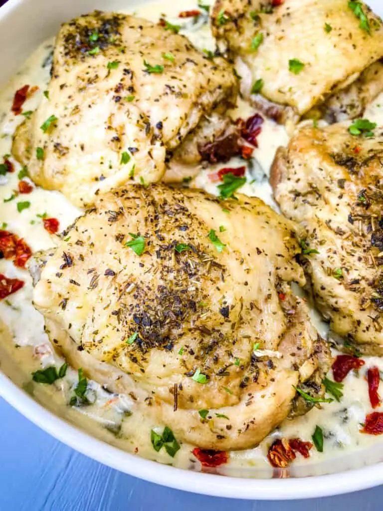 close up photo of Instant Pot Low-Carb Creamy Garlic Tuscan Chicken Thighs in creamy sauce with parsley held with tongs