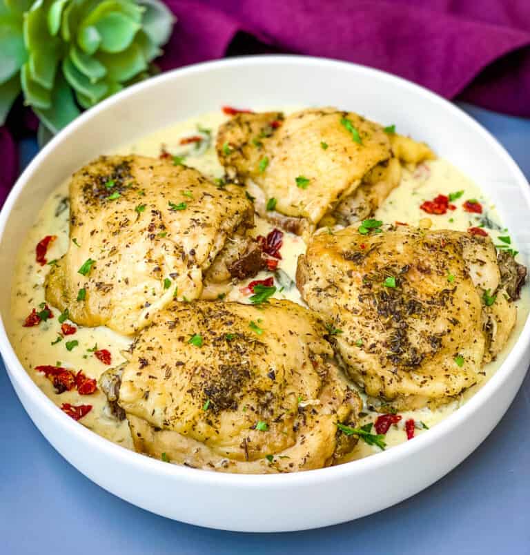 Instant Pot Low-Carb Creamy Garlic Tuscan Chicken Thighs in creamy sauce with parsley in a blue bowl