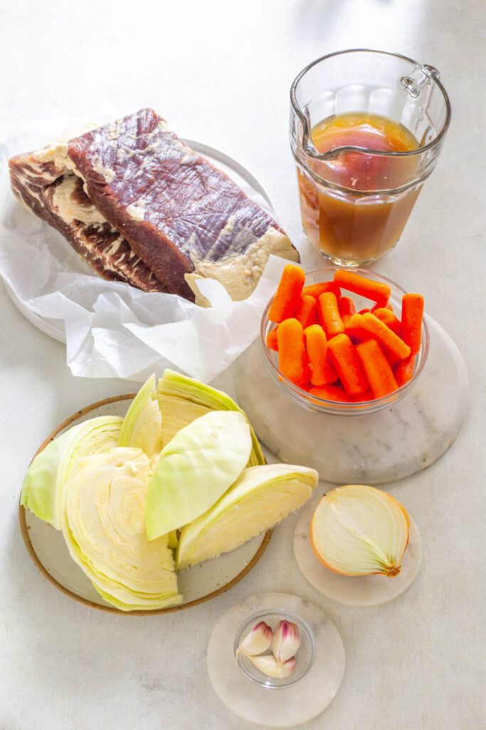 raw corned beef, fresh cabbage, fresh carrots, garlic, and broth on a flat surface