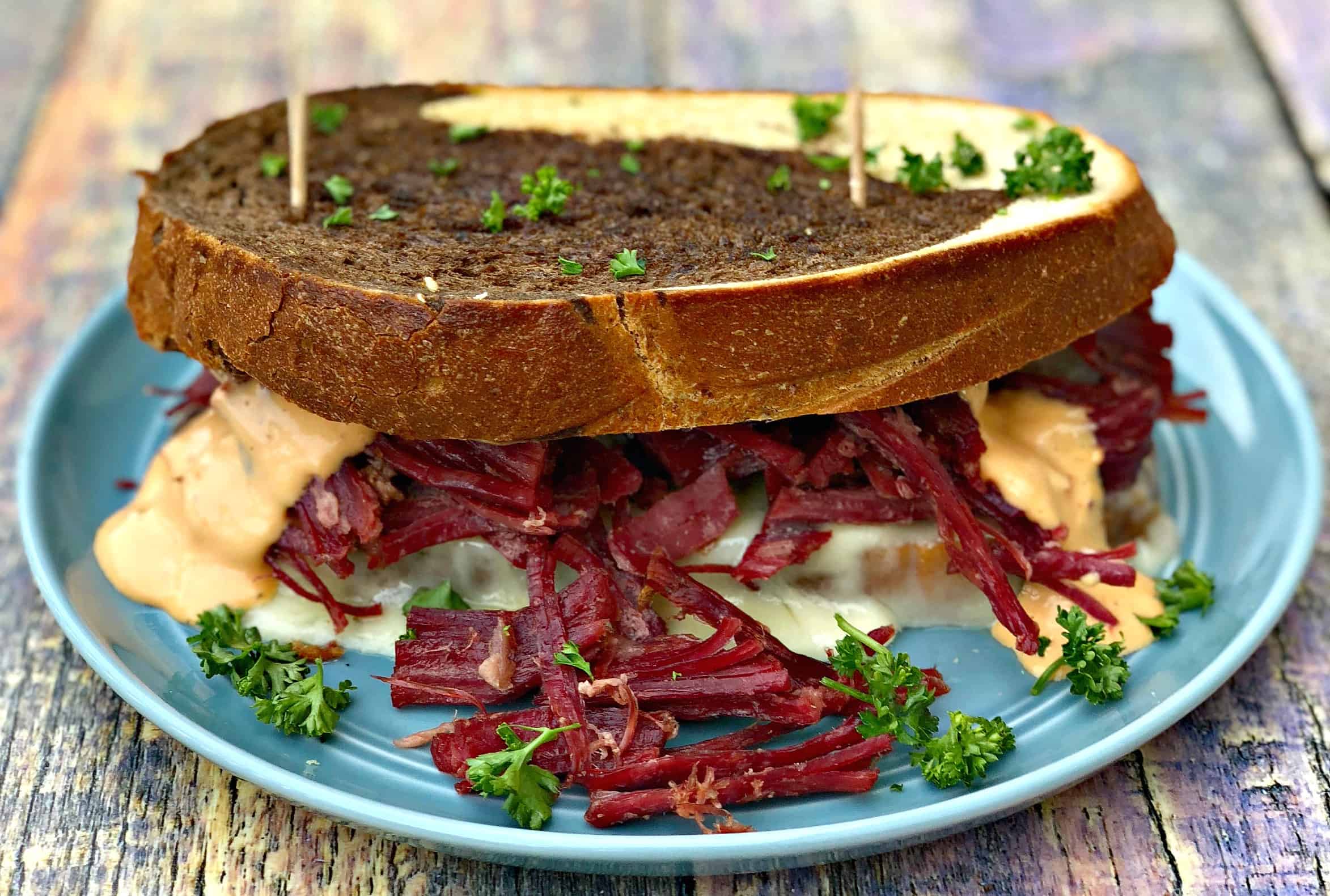 close up of Instant Pot Corned Beef Reuben Sandwich with rye bread, sauerkraut, and thousand island dressing on a blue plate