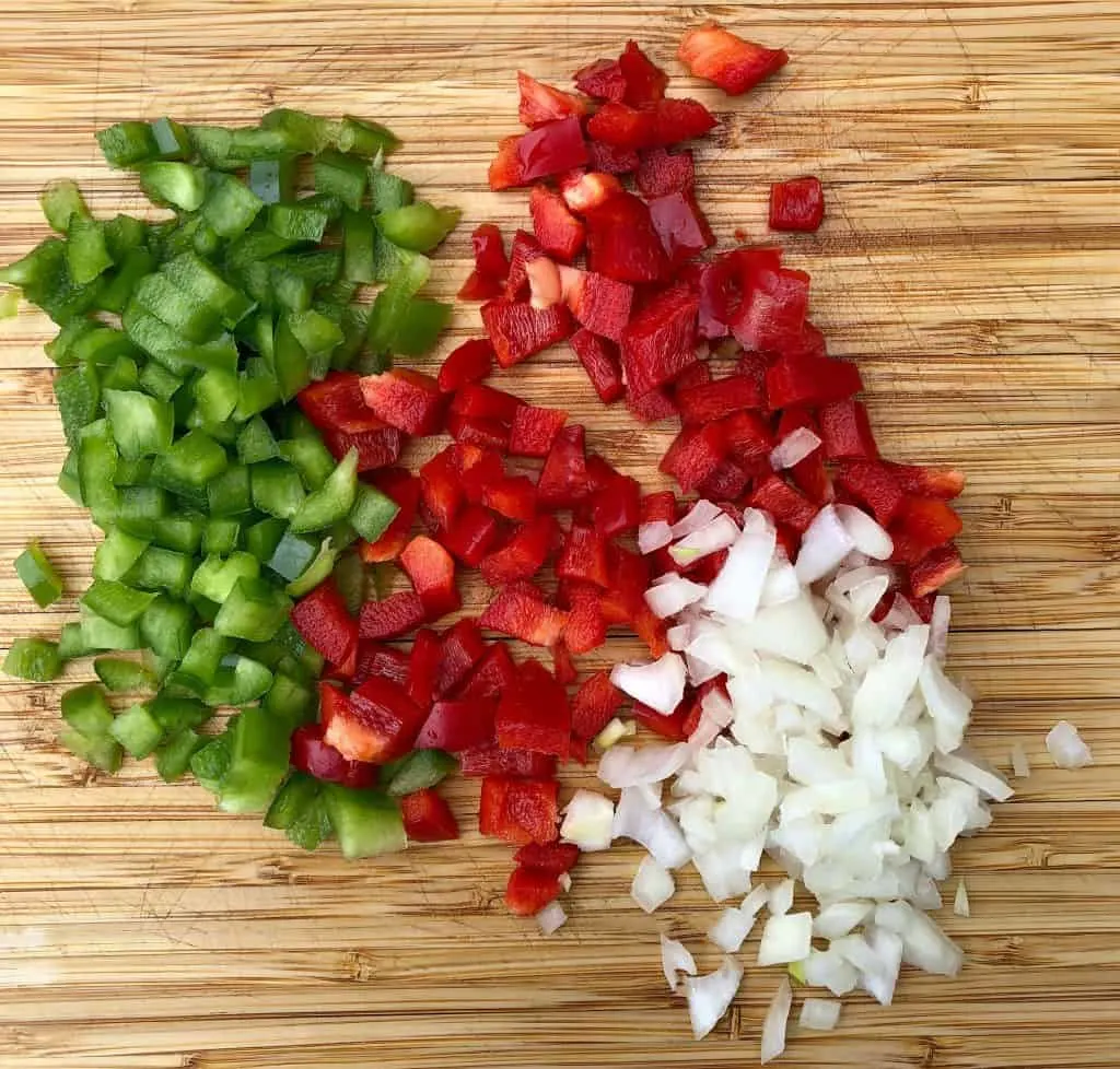 chopped red and green peppers and chopped onions on a cutting board