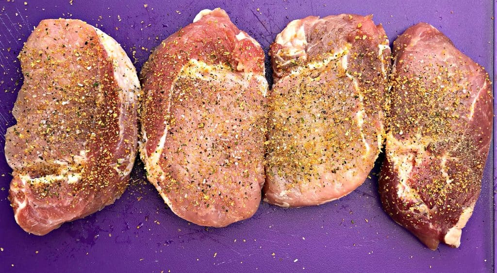 raw pork chops seasoned on a cutting board