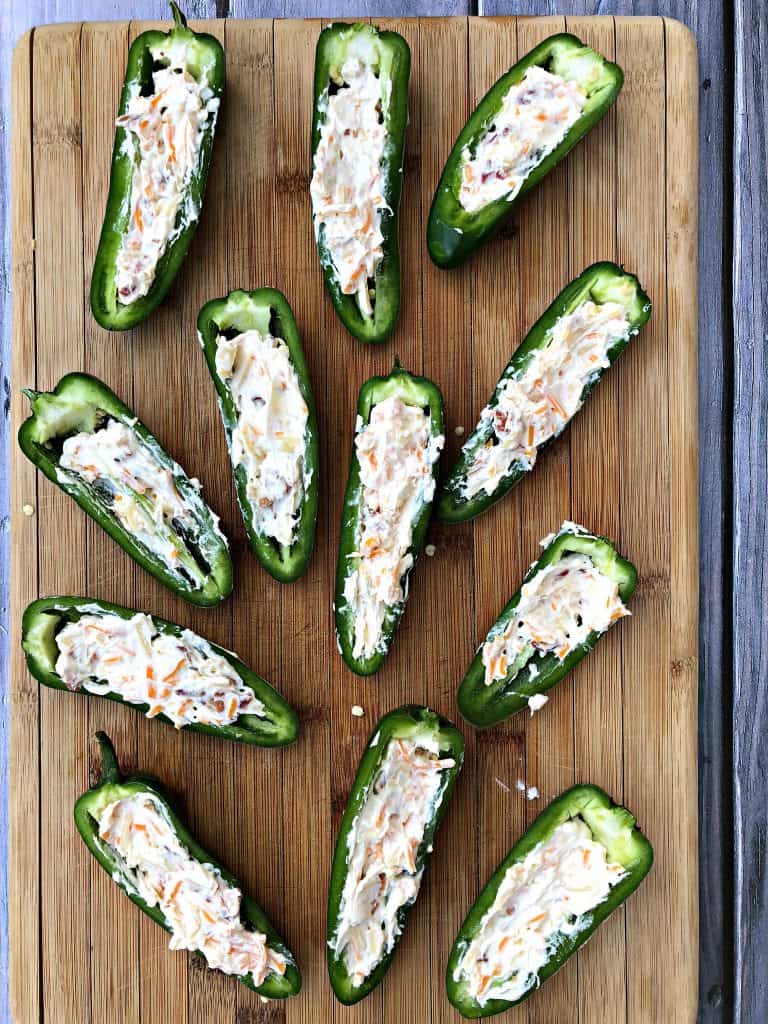 fresh jalapenos sliced in half on a cutting board stuffed with cheese